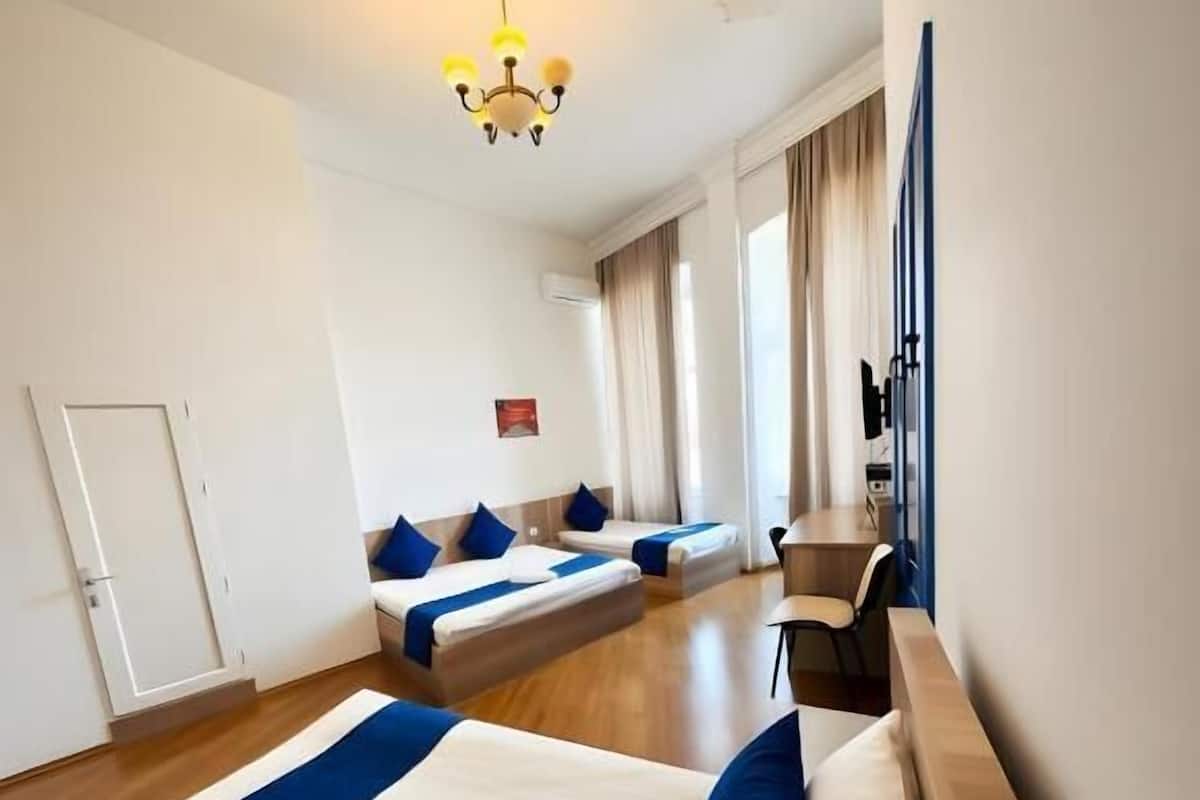 Habitació d'hotel amb dos llits, un escriptori, una cadira, una pèndol i una finestra amb cortines.