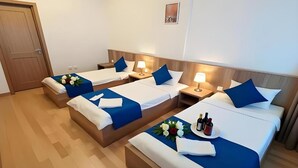 Ett hotellrum med tre sängar, var och en med ett blått överkast och vita sängkläder, ett nattduksbord med en lampa och ett litet bord med en blomsteruppsättning och flaskor.