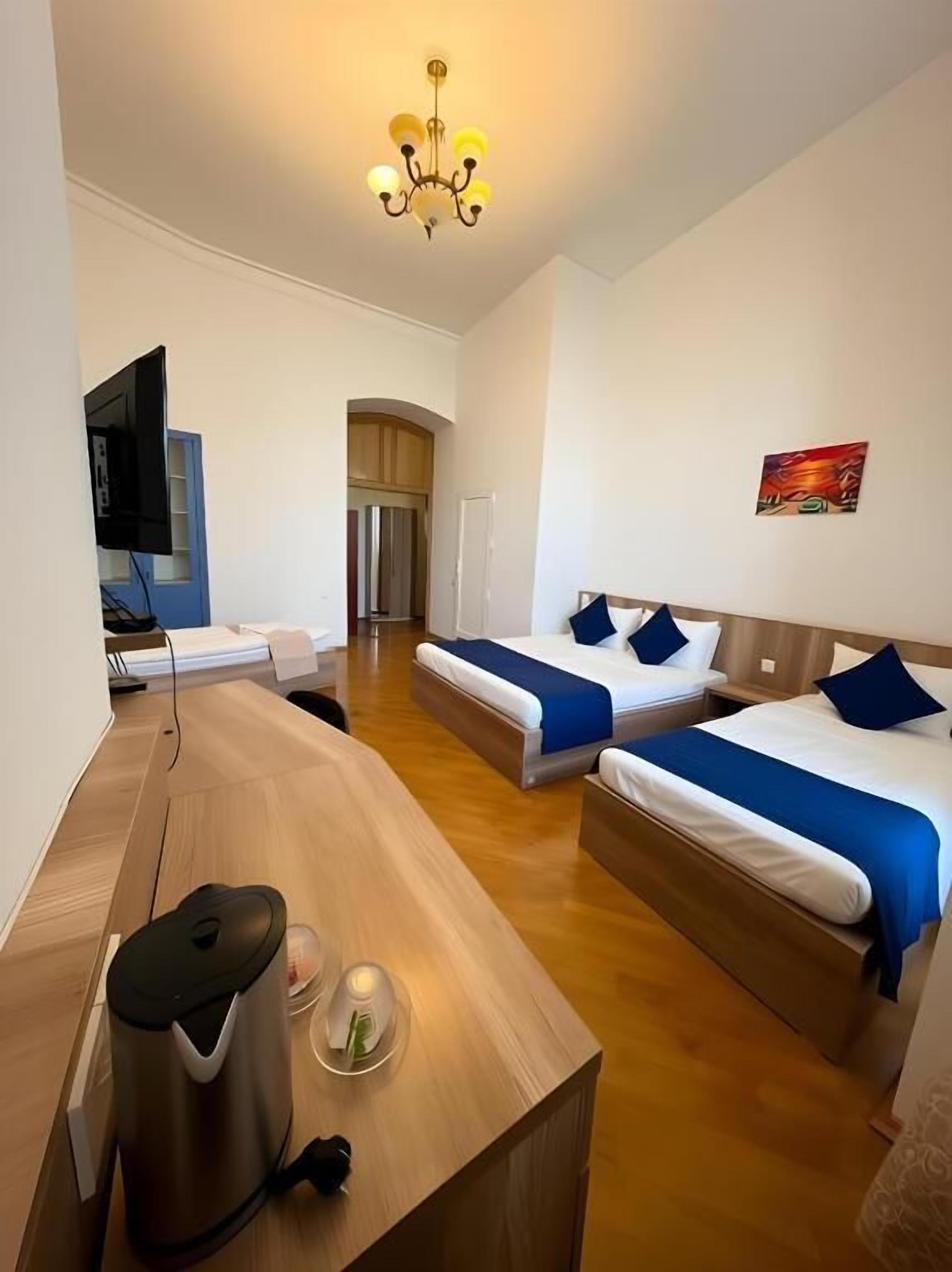 Ein Hotelzimmer mit zwei Betten, einem Schreibtisch, einem Fernseher und einem Kronleuchter.