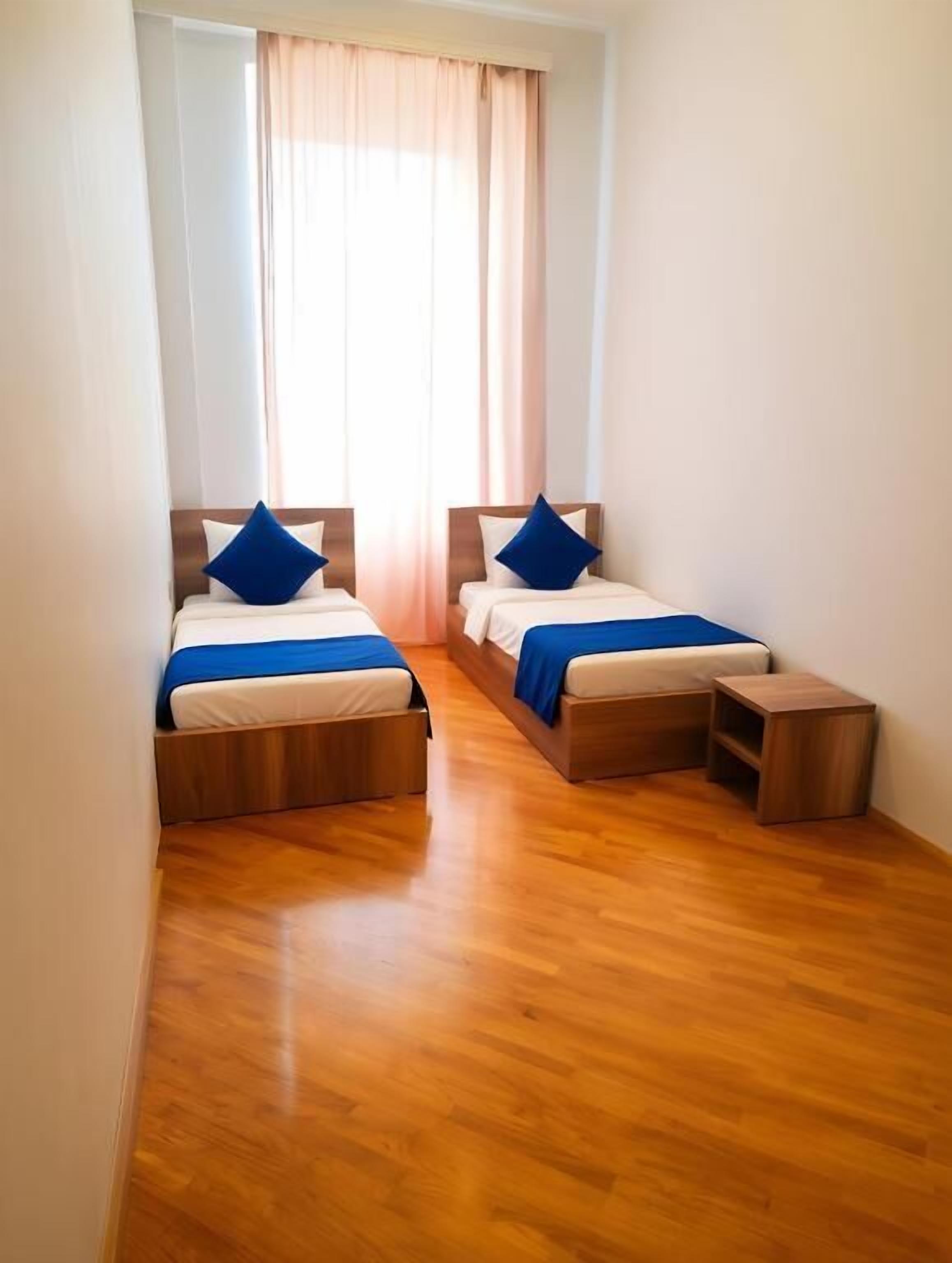Une chambre avec deux lits, un plancher en bois et une fenêtre avec des rideaux.
