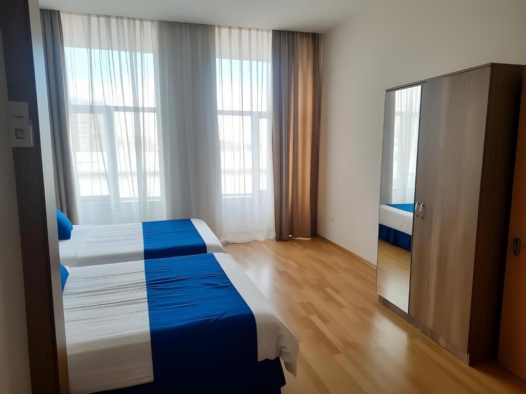 A hotel room with two beds, a wardrobe, and a large window with curtains.