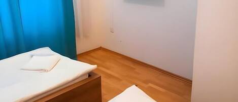 A hotel room with a bed, a bedside table, a TV mounted on the wall, and a window with blue curtains.