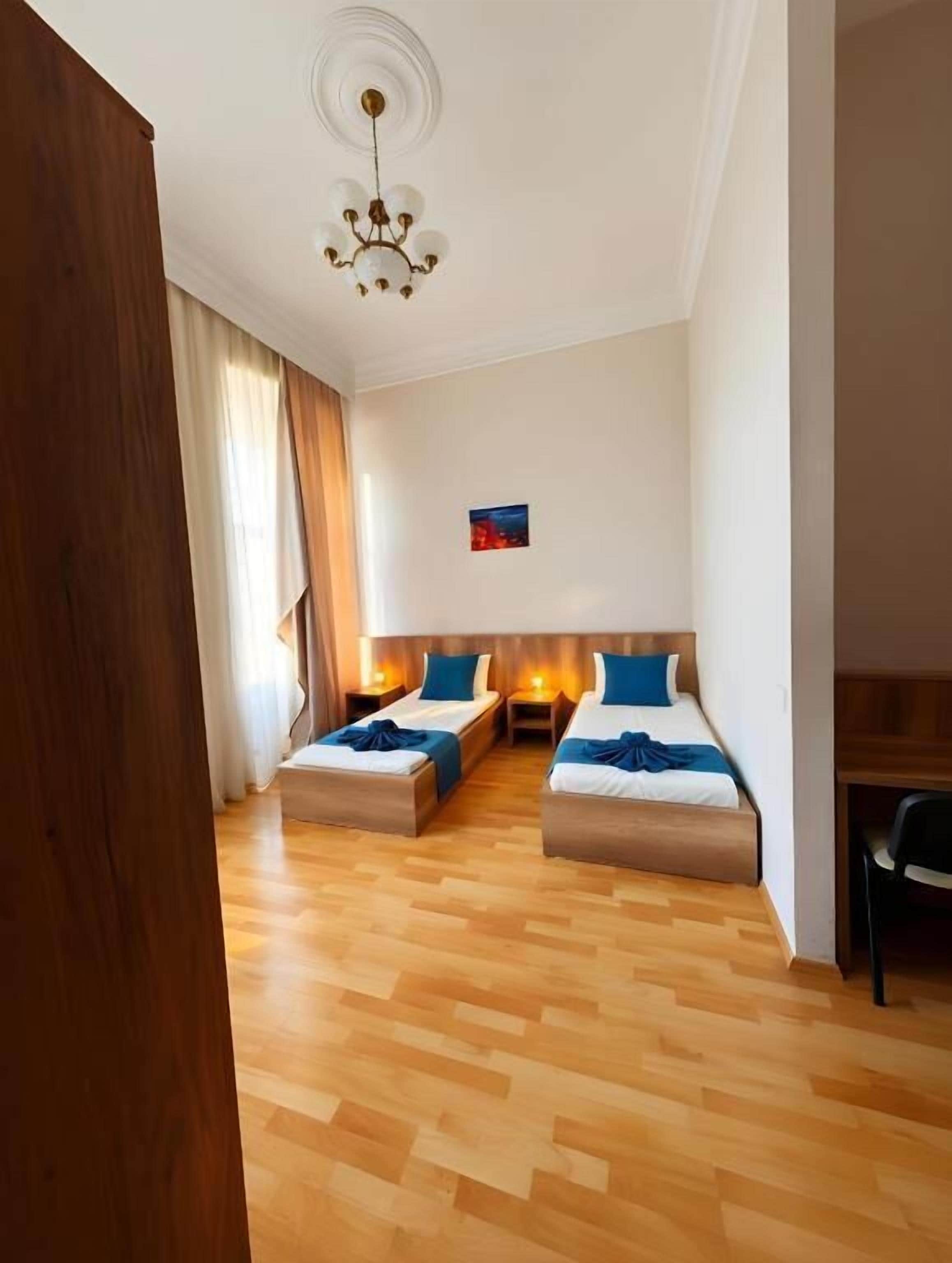 Une chambre avec deux lits, un plancher en bois, un lustre et un petit tableau accroché au mur.