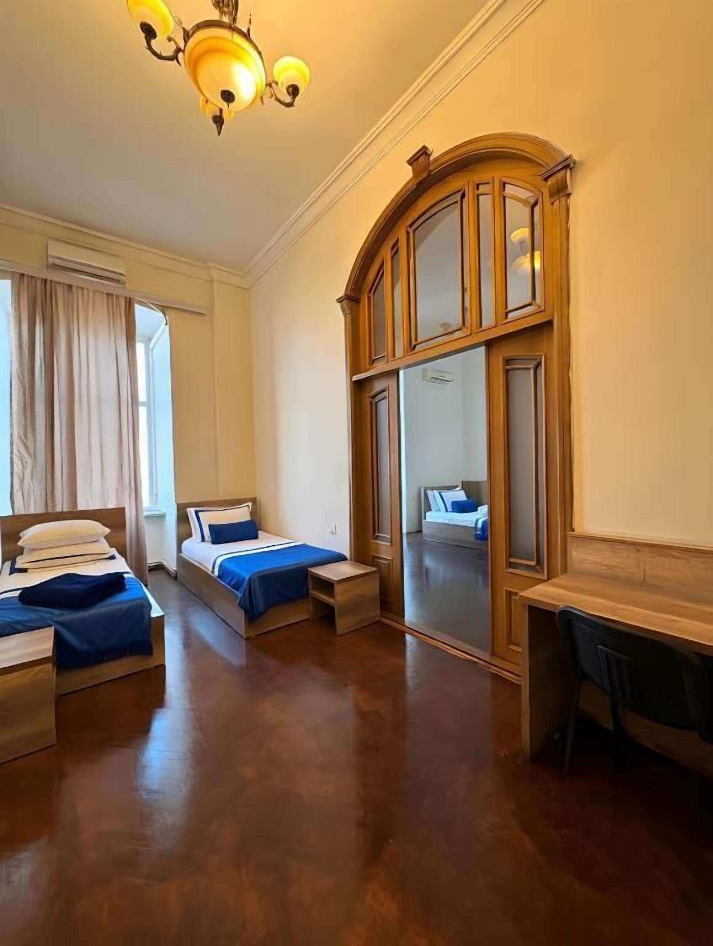 A hotel room with two beds, a desk, a mirror, and a chandelier.