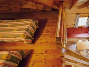 A cabin interior with a loft bed, a lower bunk, a small dining area, and a window with curtains.