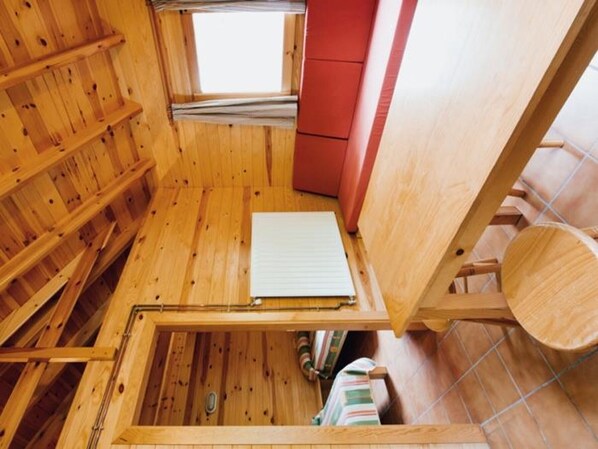 Interior de madera con techo inclinado, una ventana y un armario rojo.