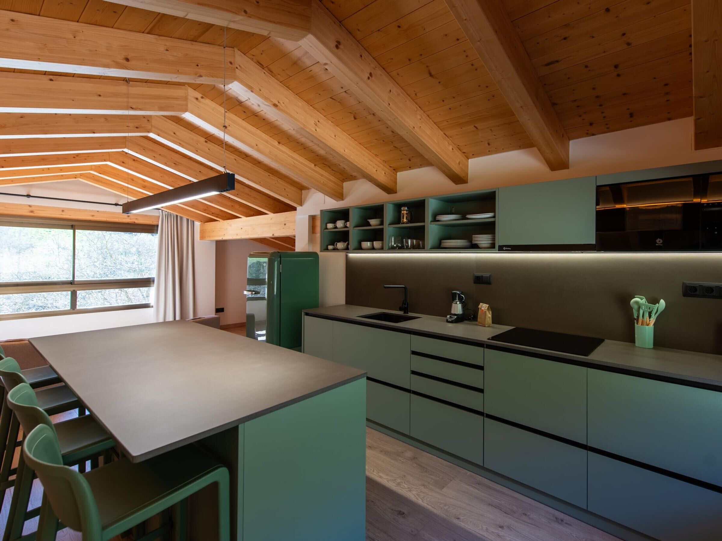 A modern kitchen with wooden beams, a central island, bar stools, and a view of the outdoors.