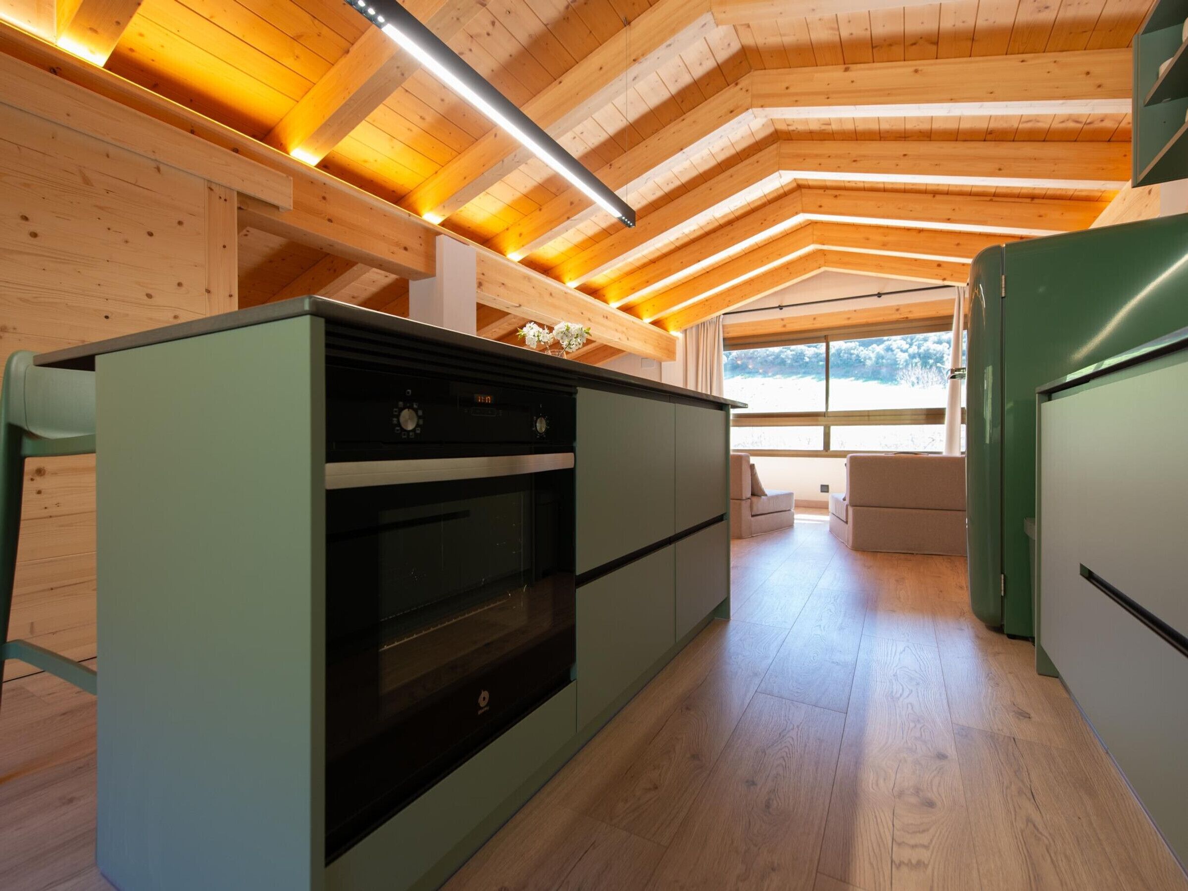Una cocina moderna con horno empotrado, techo de madera y ventanas amplias.
