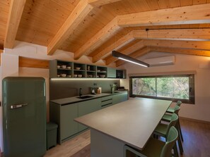 Een moderne keuken met houten balken, een groot eiland en een raam met uitzicht op bomen.