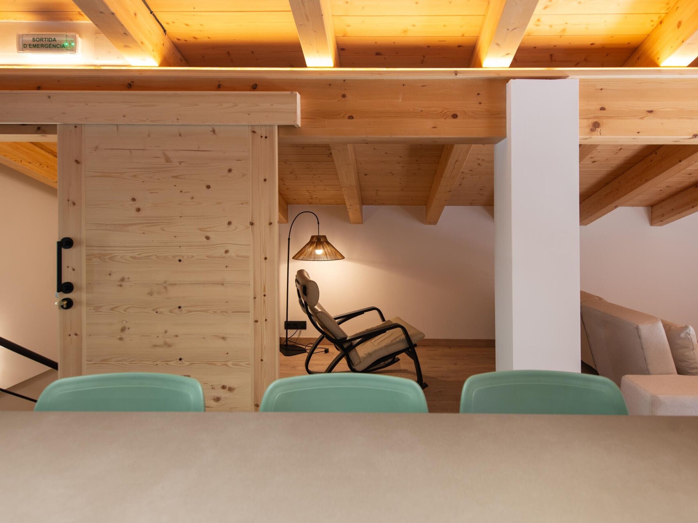 A room with a wooden ceiling, a chair, a table, and a sofa.
