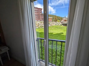 Ein Zimmer mit einer Schiebeglastür, die auf einen Balkon mit Rasenfläche und einer Steinmauer führt.