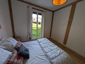 Ein Schlafzimmer mit einem großen Bett, einem Fenster mit Vorhängen, einem Nachttisch und Blick auf eine grüne Außenanlage.
