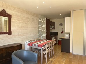 A dining area with a wooden table, chairs, a clock, and a kitchen in the background. - Cozy apartment in the heart of Cauterets - 4 guests (Cauterets)