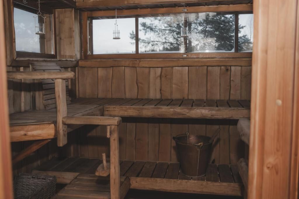 L’intérieur d’une cabane en bois, avec une fenêtre, des bancs en bois, un seau en métal et une lanterne suspendue.