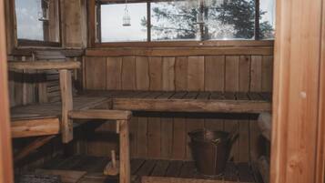 L’intérieur d’une cabane en bois, avec une fenêtre, des bancs en bois, un seau en métal et une lanterne suspendue.