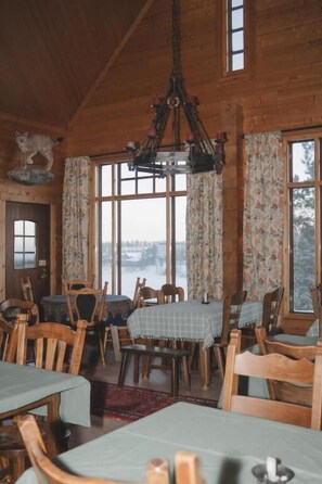 A wooden interior with a chandelier, dining tables, chairs, and large windows. - Passoo - Boutique hotel & sauna (Tahkovuori)