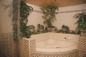 Un baño con bañera independiente, paredes de azulejos y plantas en macetas.