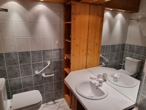 Ein Badezimmer mit Toilette, Waschbecken, Spiegel und einem Holzregal.