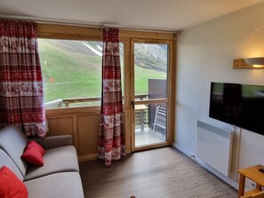 A room with a sofa, a television, a sliding glass door leading to an outdoor area, and a wooden table. - Renovated studio, pets welcome - 4 guests, slope view (Plagne Aime 2000)