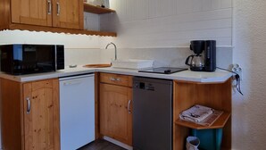 Kompakti keittiö, jossa on puukalusteet, astianpesukone, mikroaaltouuni, kahvinkeitin ja pieni hylly, jossa on sanomalehtiä.