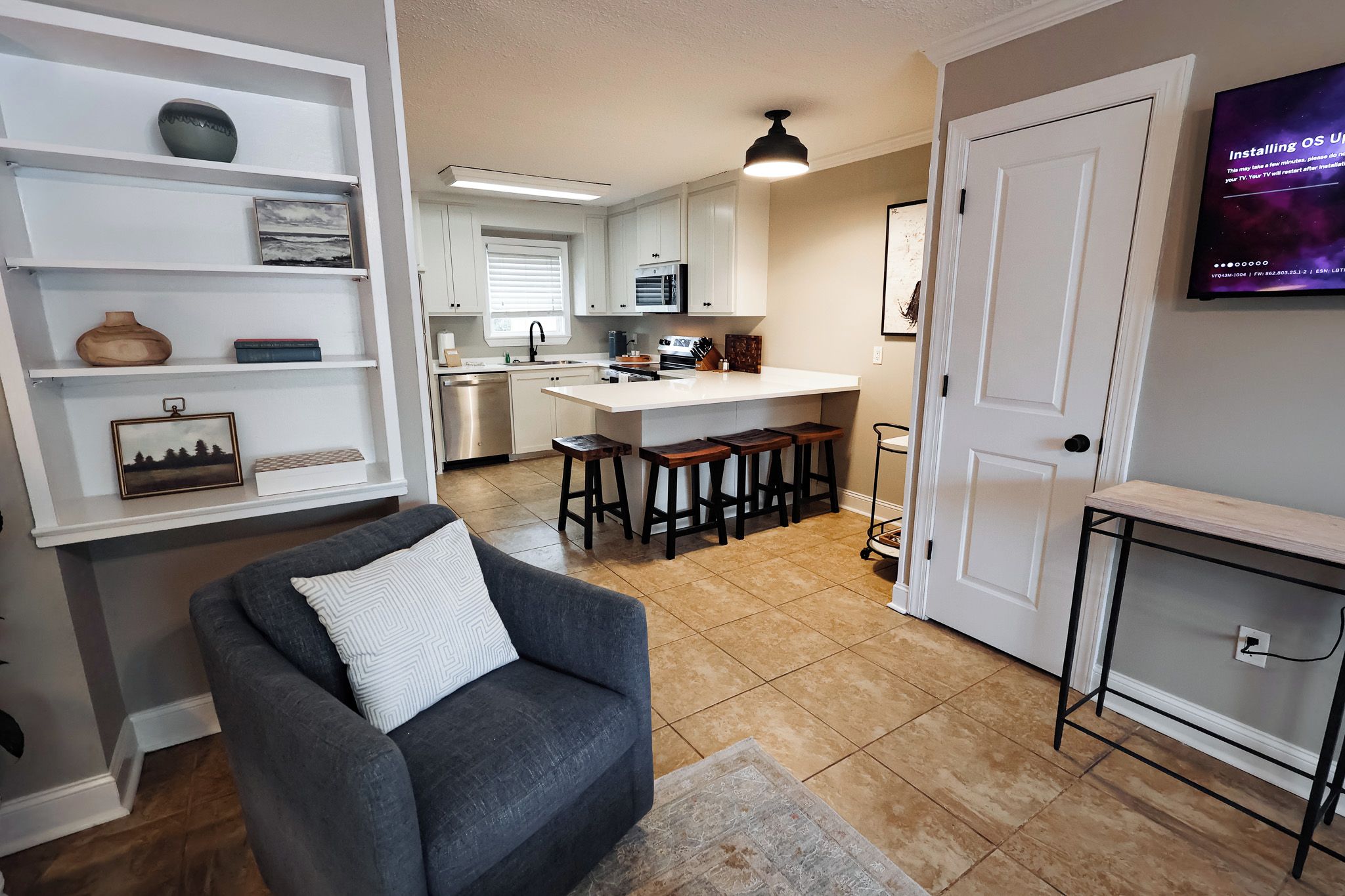 A modern kitchen with white cabinets, a dining area with bar stools, and a TV mounted on the wall.