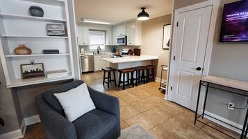 A modern kitchen with white cabinets, a dining area with bar stools, and a TV mounted on the wall.