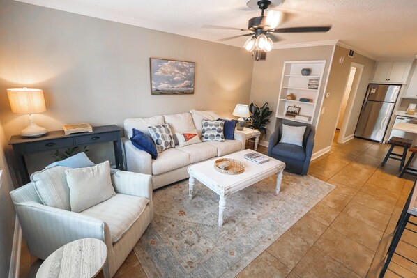A living room with a sofa, armchairs, a coffee table, and a ceiling fan.