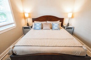 A neatly made bed with a headboard, two bedside tables with lamps, and a window with blinds.