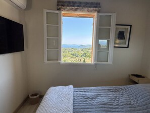 A bedroom with a bed, a window with open shutters, a television on the wall, and a framed picture. - Mas with sea view - 3 guests (La Croix-Valmer)