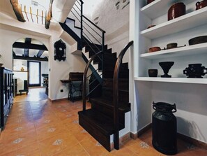 A staircase with a black handrail leading to a landing, a white wall with shelves holding pottery, and a patterned floor.