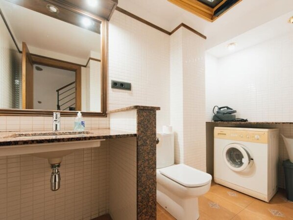 A bathroom with a sink, mirror, toilet, and washing machine.
