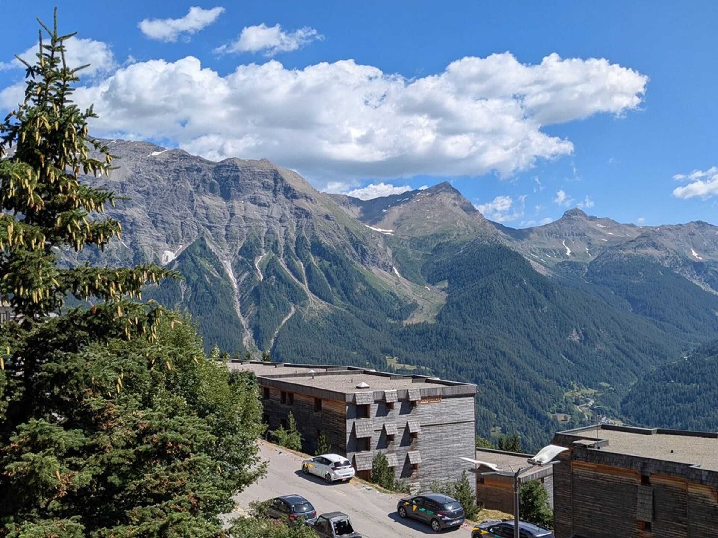 Ein Berggasthof mit Parkplatz, ein Gebäude mit markanter, geometrischer Fassade und Blick auf die umliegenden Berge.