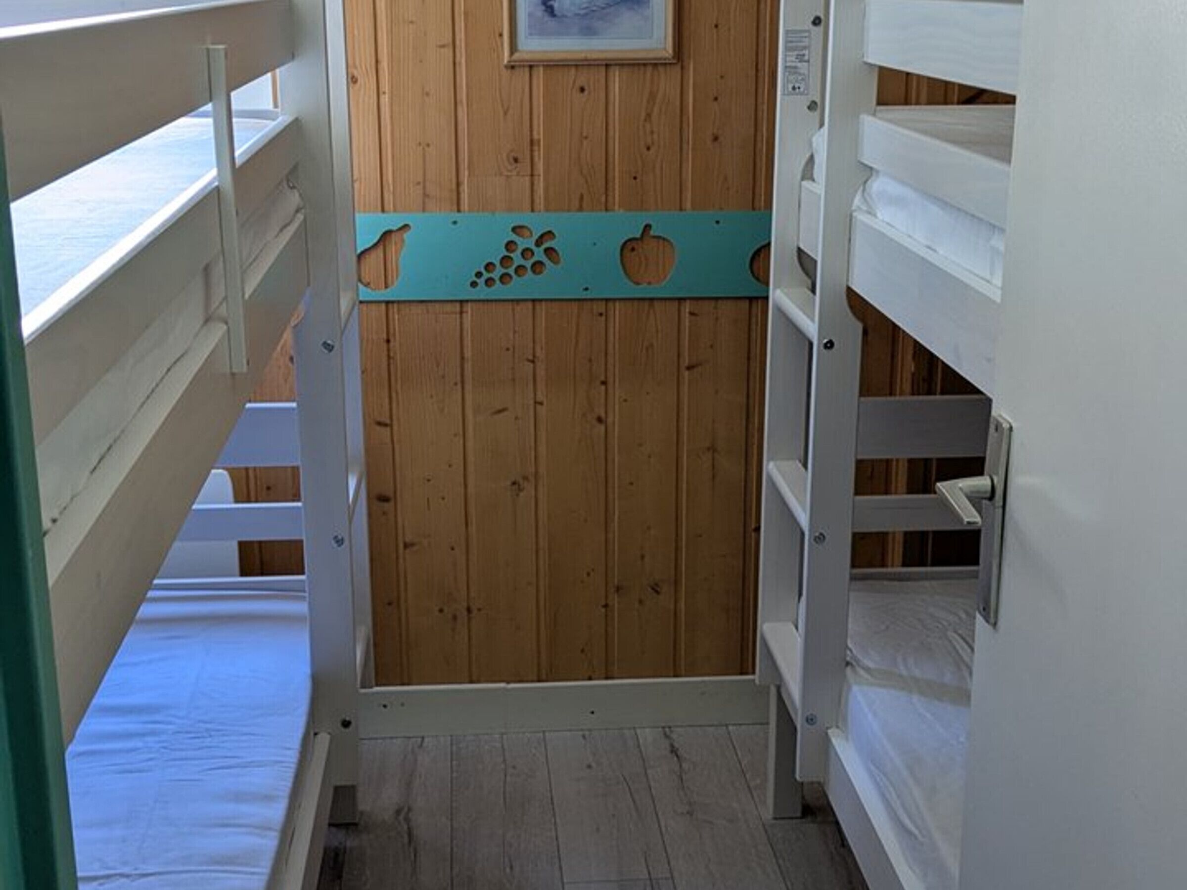 A narrow hallway with wooden walls and white railings, leading to bunk beds.