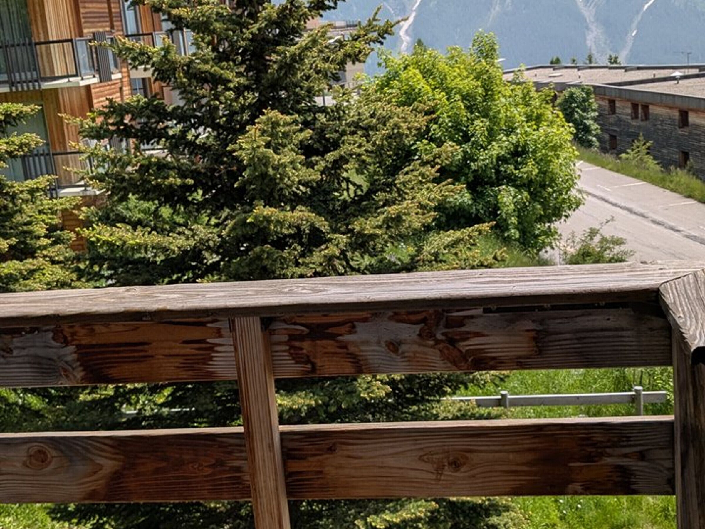 Ein Holzzaun mit Metallgitterstäben, eine Straße und üppiges Grün im Hintergrund.