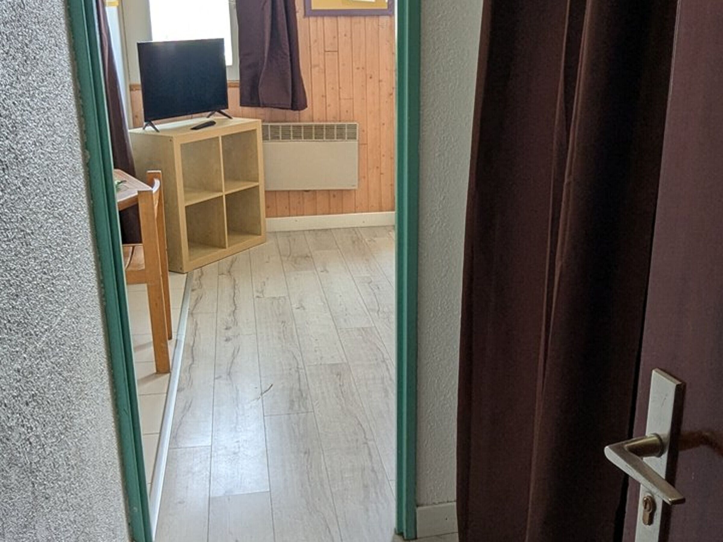 En hall med trägolv, en tv på ett tv-bord och ett element.