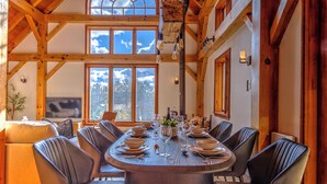 A dining area with a large round table, multiple chairs, and a view of the outdoors through large windows.