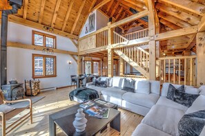 A spacious living area with a high ceiling, wooden beams, a fireplace, and a large sofa.