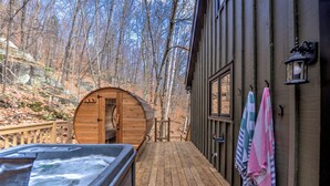 A wooden deck leading to a cabin with a hot tub and towels hanging on the wall.