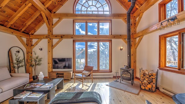 A spacious loft-style room with a high ceiling, large windows, a fireplace, and a cozy seating area.