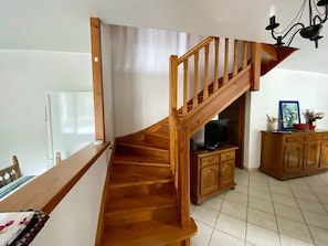 Eine Holztreppe führt zu einer unteren Ebene, einem Essbereich mit Tisch und Stühlen sowie einem Schrank mit einem Fernseher.