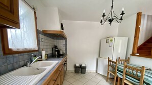 Una cocina con dos fregaderos, un refrigerador, una araña y una mesa de comedor con sillas.