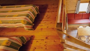 Ein Blockhaus-Interieur mit Schlafkoje, einer unteren Schlafflache, einer kleinen Essecke und einem Fenster mit Vorhängen.