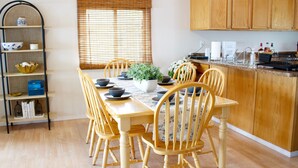 A dining area with a wooden table, chairs, a potted plant, and a kitchen area with wooden cabinets. - Inviting Lakefront Escape with Modern Comforts & High‑Speed Fiber (Edgerton)