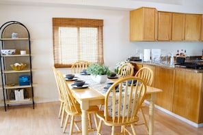 Un comedor con una mesa de madera, sillas, una planta en maceta y una cocina con armarios de madera.