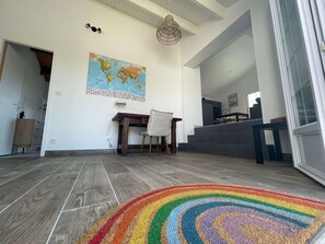 A spacious living area with a wooden floor, a world map on the wall, a dining table with chairs, and a staircase leading to an upper level. - Welcoming house near the beach - 6 guests (L'Épine)