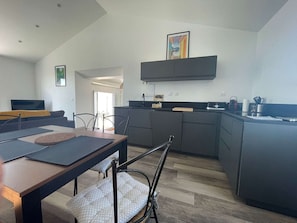 A modern kitchen with dark cabinetry, a dining area with a wooden table and chairs, and a small island with a sink. - Welcoming house near the beach - 6 guests (L'Épine)