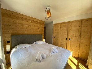 Un dormitorio con cabecera de madera, una cama grande con ropa de cama blanca, dos toallas enrolladas, una lámpara de noche y armarios de madera.