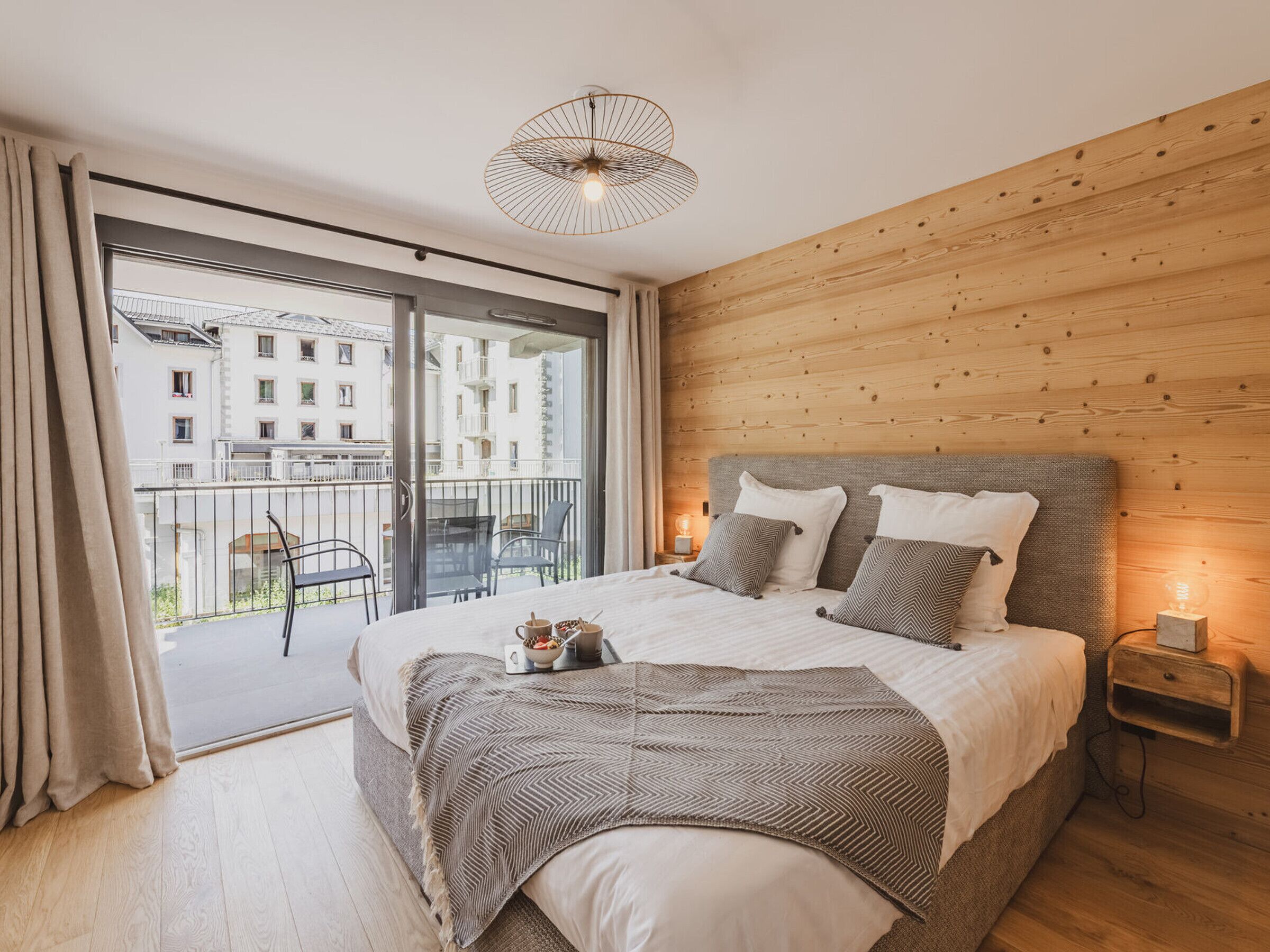 Ein Schlafzimmer mit einem großen Bett, einem Holz-Kopfteil, einem Balkon mit Stühlen und Blick auf Gebäude.