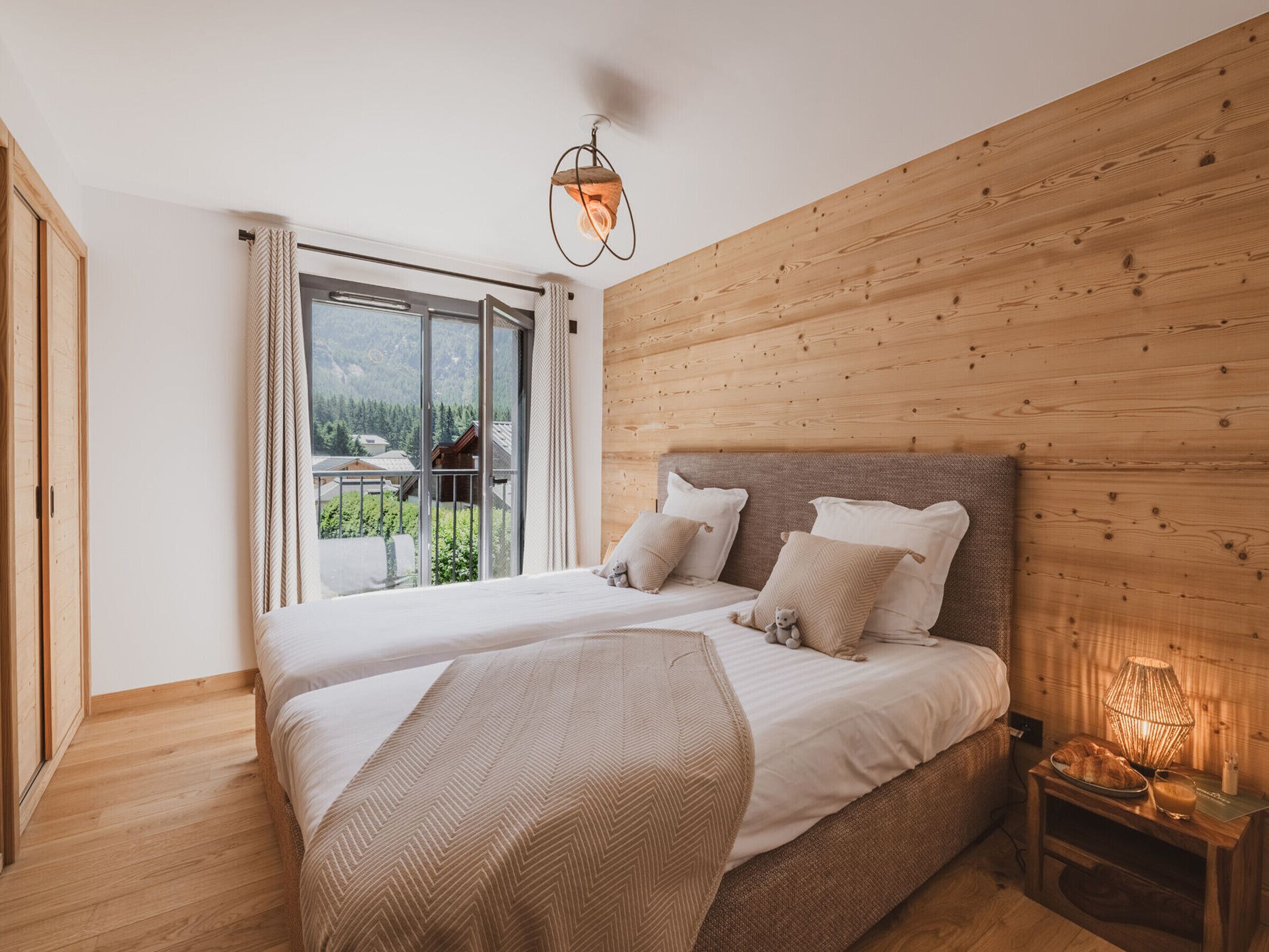 Une chambre à coucher avec un grand lit, une tête de lit en bois, une table de chevet avec une lampe et une vue sur un balcon.