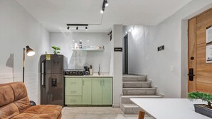 Eine kleine Küche mit Kühlschrank, Herd und grünen Schränken. Ein Essbereich mit Tisch und braunem Sofa.